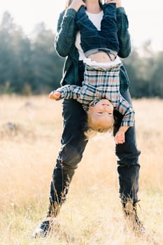 Mom holds the legs of a little smiling girl upside down in the meadow. Cropped. High quality photo