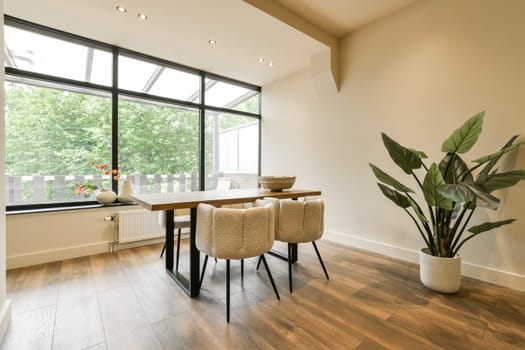 a dining table and chairs in a room with large windows looking out onto the trees outside on a sunny day