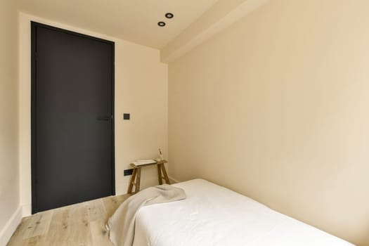 a room with a bed and a black door in the corner to the left is an empty chair on the right side