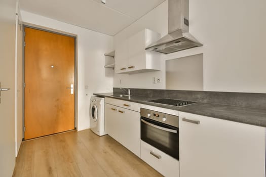 a kitchen area with white cabinets and wood flooring in the center of the room, there is a washer on the right