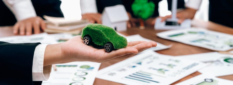 Businessman holding green EV car model mock in electric car company meeting, business people planning strategic marketing for eco-friendly vehicle product using clean energy with net zero.Trailblazing