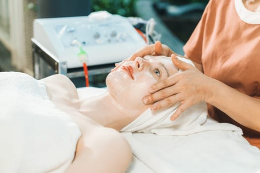 Portrait of beautiful caucasian woman having facial massage with homemade facial mask while lies on spa bed surrounded by beauty electrical equipment and peaceful nature environment. Tranquility.