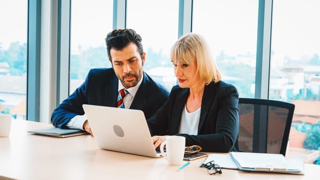 Two business people talk project strategy at office meeting room. Businessman discuss project planning with colleague at modern workplace while having conversation and advice on financial report. Jivy