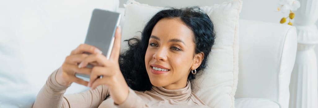 Relaxed young African American woman using crucial mobile phone on sofa couch in living room at home