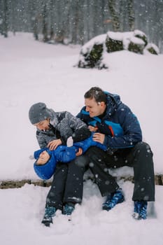 Little girl lies on her mom and dad lap and catches snow in her mouth. High quality photo