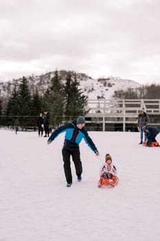 Smiling dad rides a small child on a sleigh on a snowy hill. High quality photo