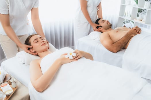 Caucasian couple enjoying relaxing anti-stress head massage and pampering facial beauty skin recreation leisure in dayspa modern light ambient at luxury resort or hotel spa salon. Quiescent