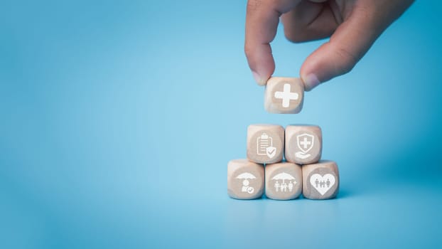 Health insurance and healthcare concept, human hand holds wooden block with icons about health insurance and healthcare access, retirement planning on blue background.