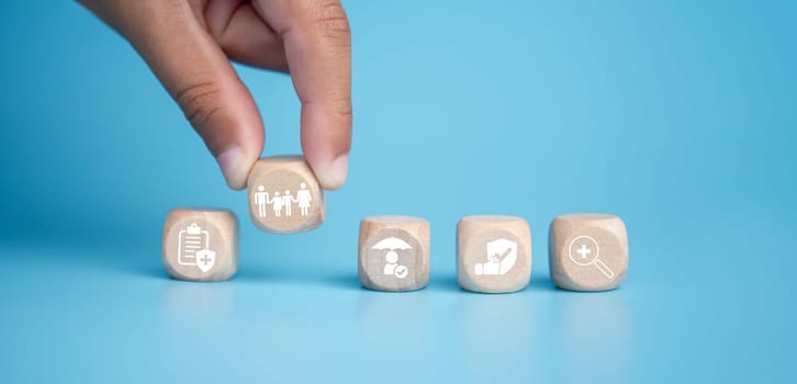Health insurance and healthcare concept, human hand holds wooden block with icons about health insurance and healthcare access, retirement planning on blue background.