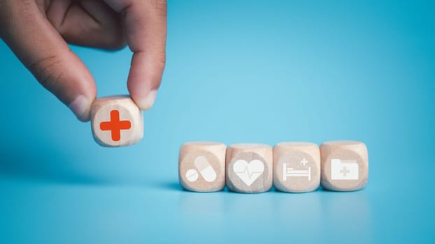 Health and medical concept Human hand holds a wooden block with icons about health and access to treatment and medicine and supplies on a blue background.