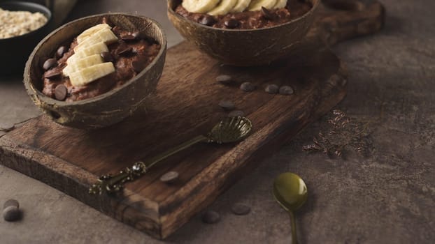 Coconut bowls with oat porridge with banana and round chocolate chips.