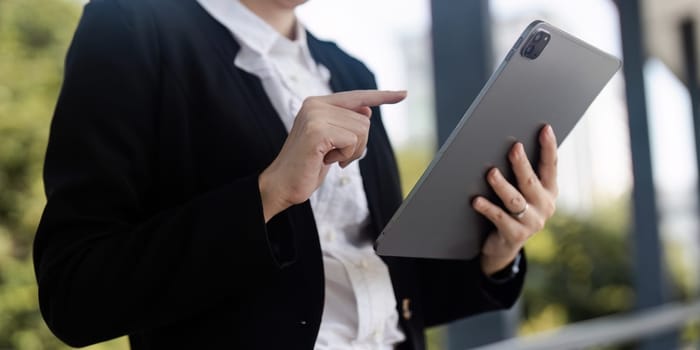 Asian business woman leader entrepreneur, professional manager holding digital tablet computer using software applications standing on the street.