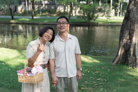 Retired couple holding hands in gardening and wife holding basket filled with flowers.