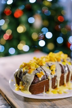 Chocolate stollen covered with icing and mandarin pieces stands on the table. High quality photo