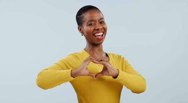 Happy black woman, portrait and heart hands for love, care or romance against a gray studio background. Face of African female person or model showing like emoji, shape or romantic gesture on mockup.