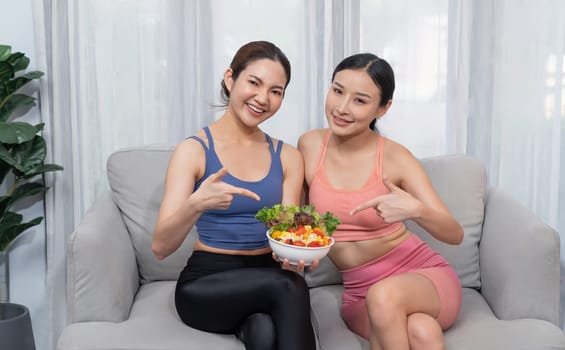 Young sporty Asian women in sportswear holding salad bowl together fill with vibrant of fruit and vegetable. Natural youthful and fit body lifestyle with balance nutrition and home exercise. Vigorous