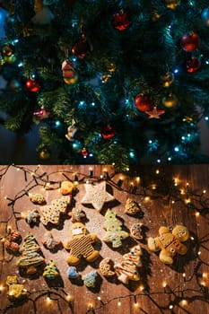 Colorful glazed cookies on a floured table among glowing garlands near festive Christmas tree. High quality photo