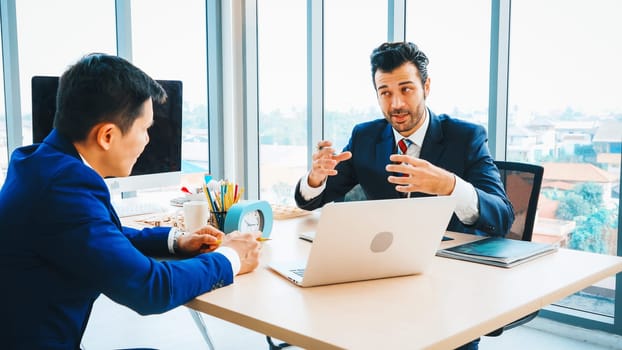 Two business people talk project strategy at office meeting room. Businessman discuss project planning with colleague at modern workplace while having conversation and advice on financial report. Jivy