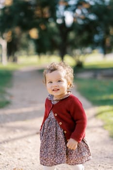 Little smiling girl stands on a dirt path in the park. High quality photo