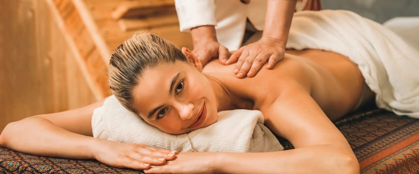 A portrait of a pretty girl having body massage while looking at camera with happiness in front of wooden sauna cabinet. Attractive blonde female feel relaxed from Thai massage. Tranquility.