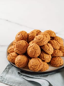 Plate of cookie amaretti on white marble background - traditional Italian Sardinian pastry. Delicious amaretti biscuit cookies made from almond or apricot kernels with copy space