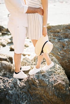 Man hugs woman around the waist while standing on boulders in the sea. Cropped. Faceless. High quality photo