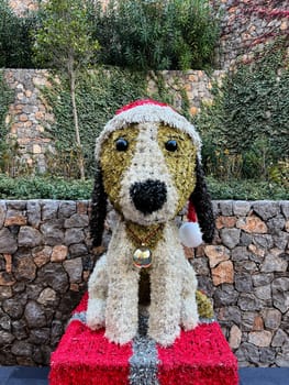Fluffy Christmas figure of a dog in a Santa hat on a pedestal in the garden. High quality photo
