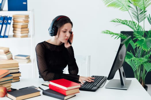 business woman office worker in headphones in office at a desk with books in the office with a laptop rescue service