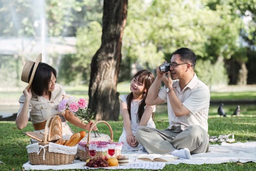 Family of senior couple and daughter picnicking in the park showing love Or reconnect after retirement in a relaxing park. An elderly man and a woman have fun on a mat in the backyard..