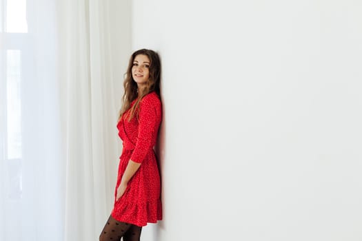 a woman in red dress stands against a white wall