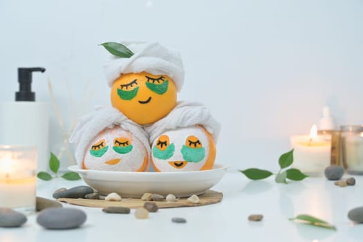 Orange fruits in face mask, zen stones, candles and green leaves on white background. Spa treatment and self care concept.