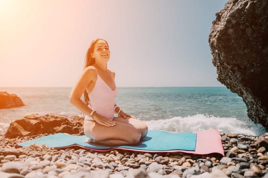 Young woman with black hair, fitness instructor in pink sports leggings and tops, doing pilates on yoga mat with magic pilates ring by the sea on the beach. Female fitness daily yoga concept