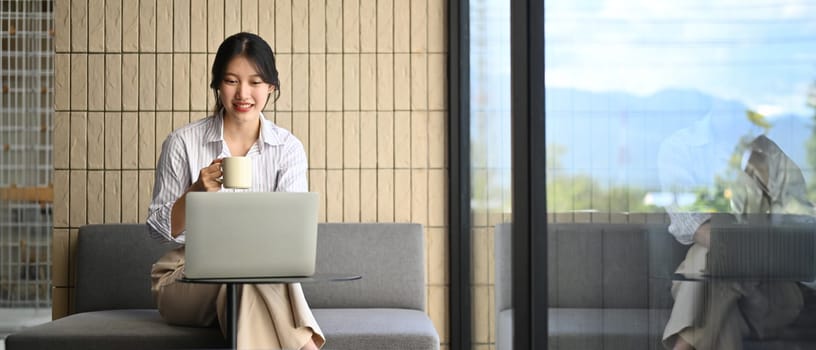 Attractive businesswoman using laptop sitting near window with a view of mountains.