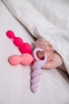 Woman holding three different anal beads while lying in bed