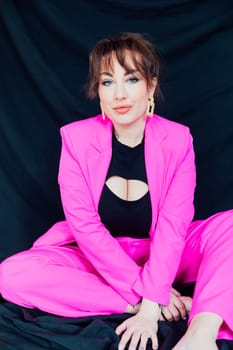 fashionable woman in bright clothes sits on a black background