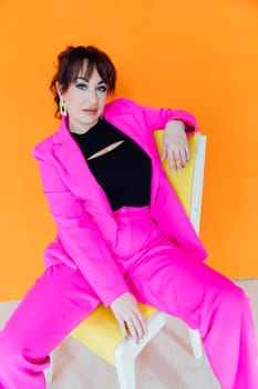 woman in bright clothes sits on a chair on an orange background