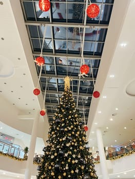Decorated with balls and garlands, a tall Christmas tree stands in a shopping center between floors. High quality photo