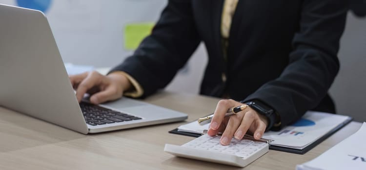 Close up, Businesswoman uses calculator to calculate finances, mathematics on table in office and business charts, tax, accounting, statistics and analytical research concept..