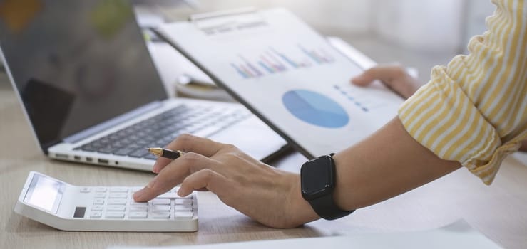 Close up, Businesswoman uses calculator to calculate finances, mathematics on table in office and business charts, tax, accounting, statistics and analytical research concept..