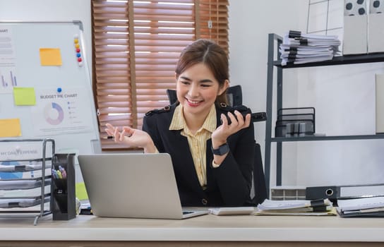 Businesswoman using laptop to do finance, talking on phone, working with numbers on wooden table in office and business background, tax, accounting, statistics and analytical research concept..