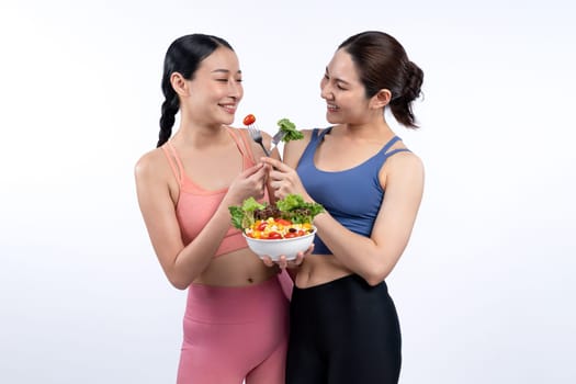 Two young sporty Asian women in sportswear holding salad bowl fill with fruit and vegetable. Natural youthful and fit body lifestyle people with balance nutrition on isolated background. Vigorous