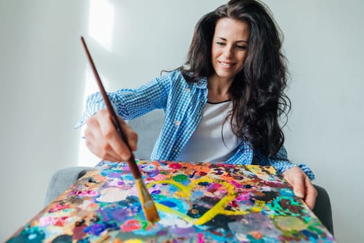 woman artist in blue clothes draws with brush on canvas