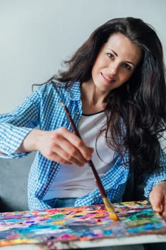 woman artist in blue clothes draws with brush on canvas