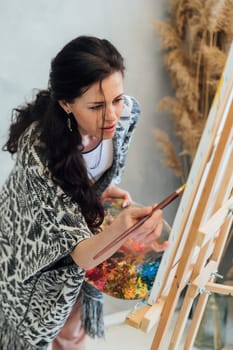 woman artist paints with brushes on a white canvas near brown flowers