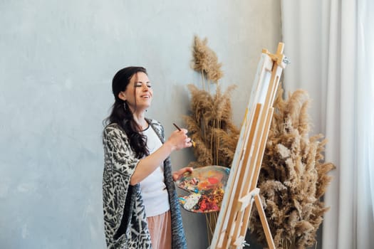 woman artist paints with brushes on a white canvas near brown flowers