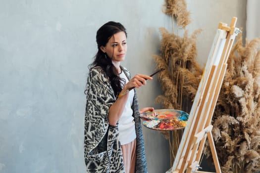 woman artist paints with brushes on a white canvas near brown flowers