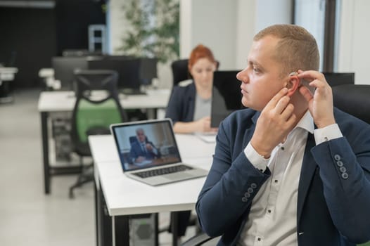Caucasian man putting on hearing aid to online meeting on laptop