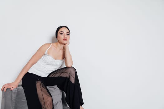 fashionable woman in a white T-shirt and black pants sits on a chair with a white background