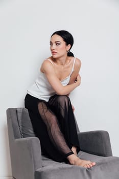fashionable woman in a white T-shirt and black pants sits on a chair with a white background