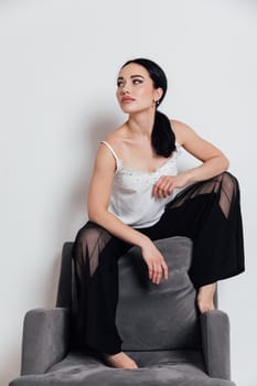 fashionable woman in a white T-shirt and black pants sits on a chair with a white background